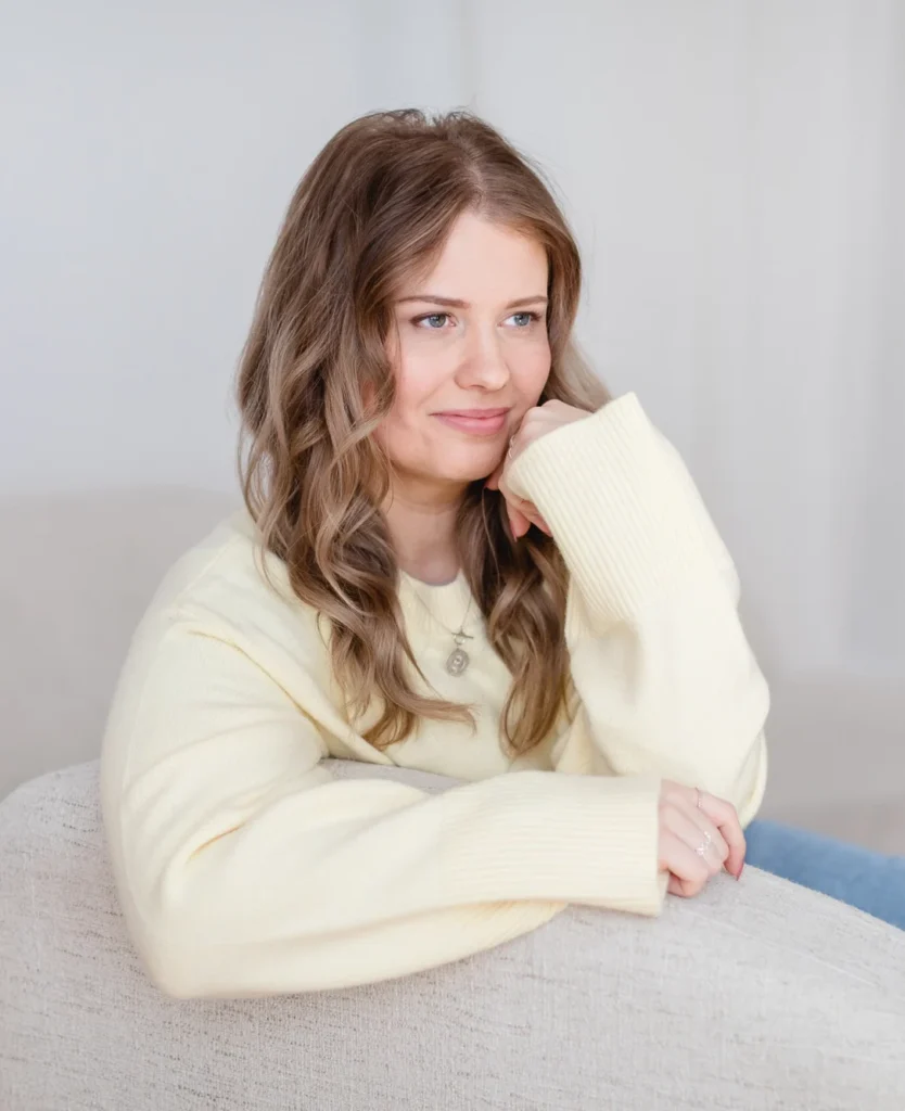 Katrin sitzt in einem hellen Sessel und blickt nachdenklich zur Seite