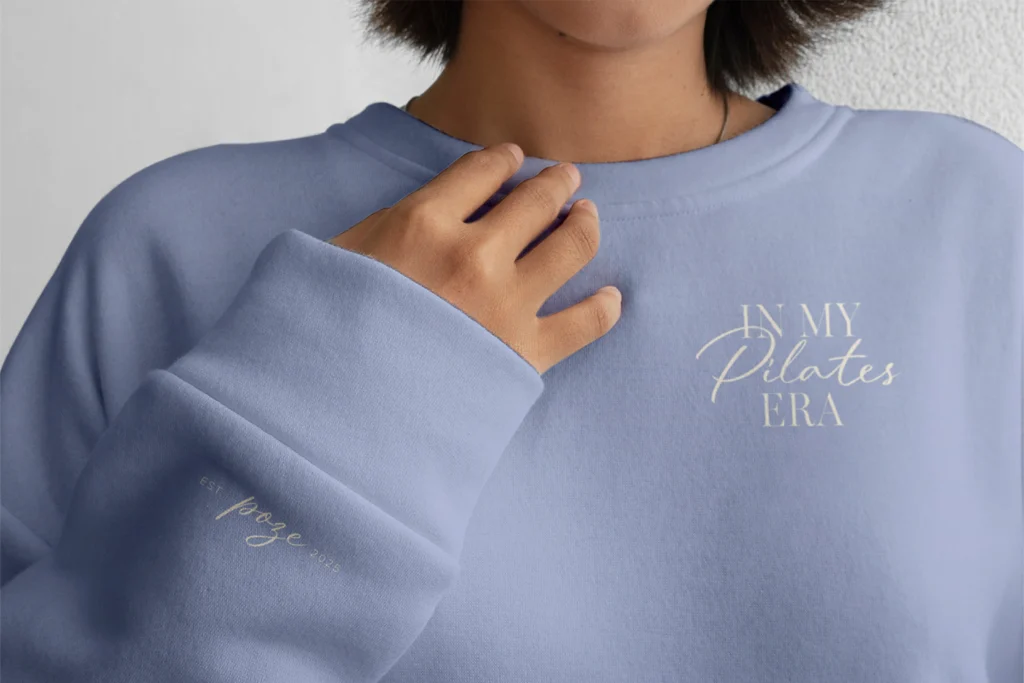 Gebrandeter Poze-Pilates-Sweater in zartem Lavendelton mit dem Slogan „In My Pilates Era“. Das Design verbindet moderne Lifestyle-Ästhetik mit der Markenidentität des Studios und richtet sich an eine engagierte Pilates-Community.